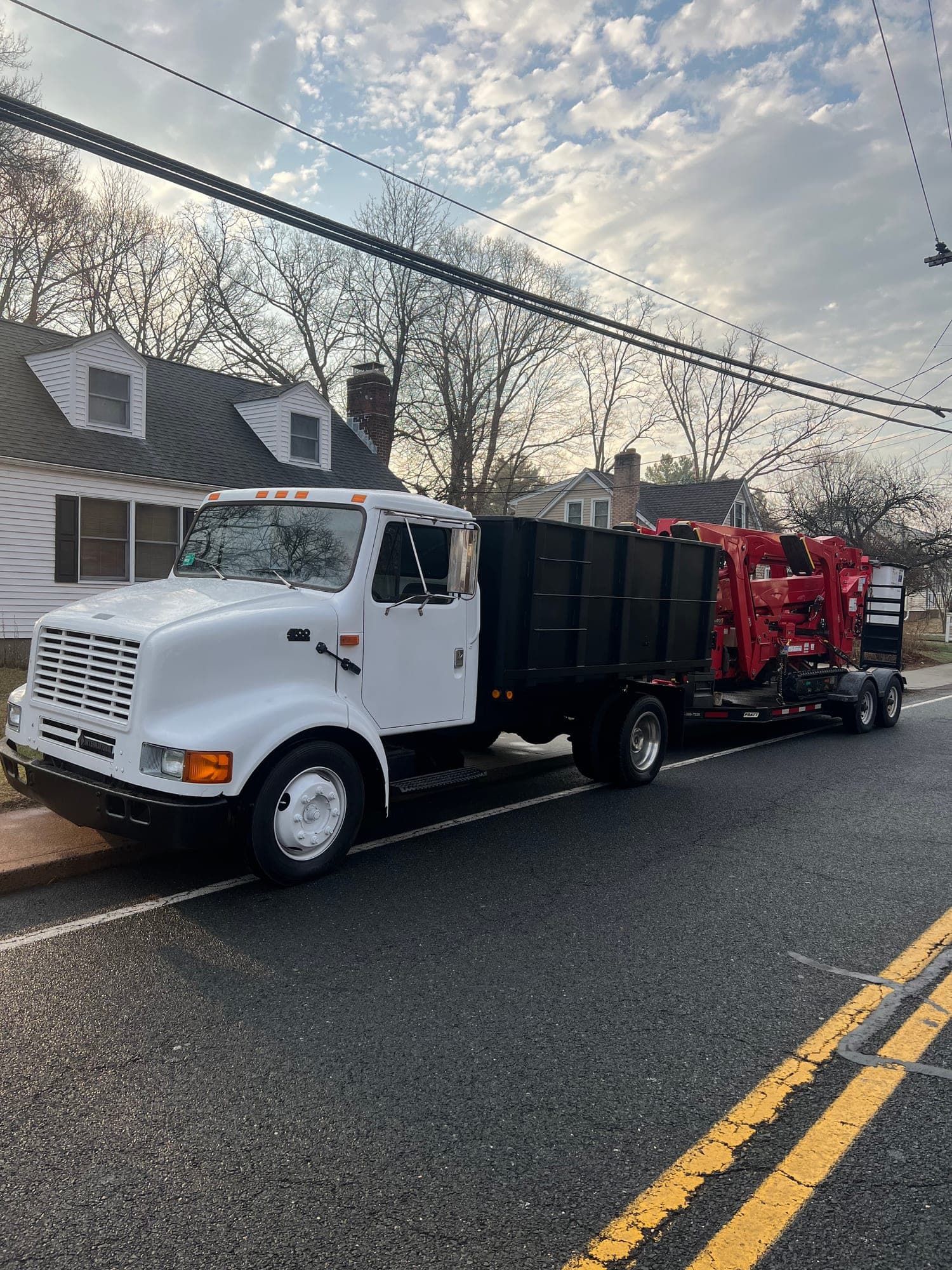 JLO Tree Service truck towing a red wood chipper down a residential road