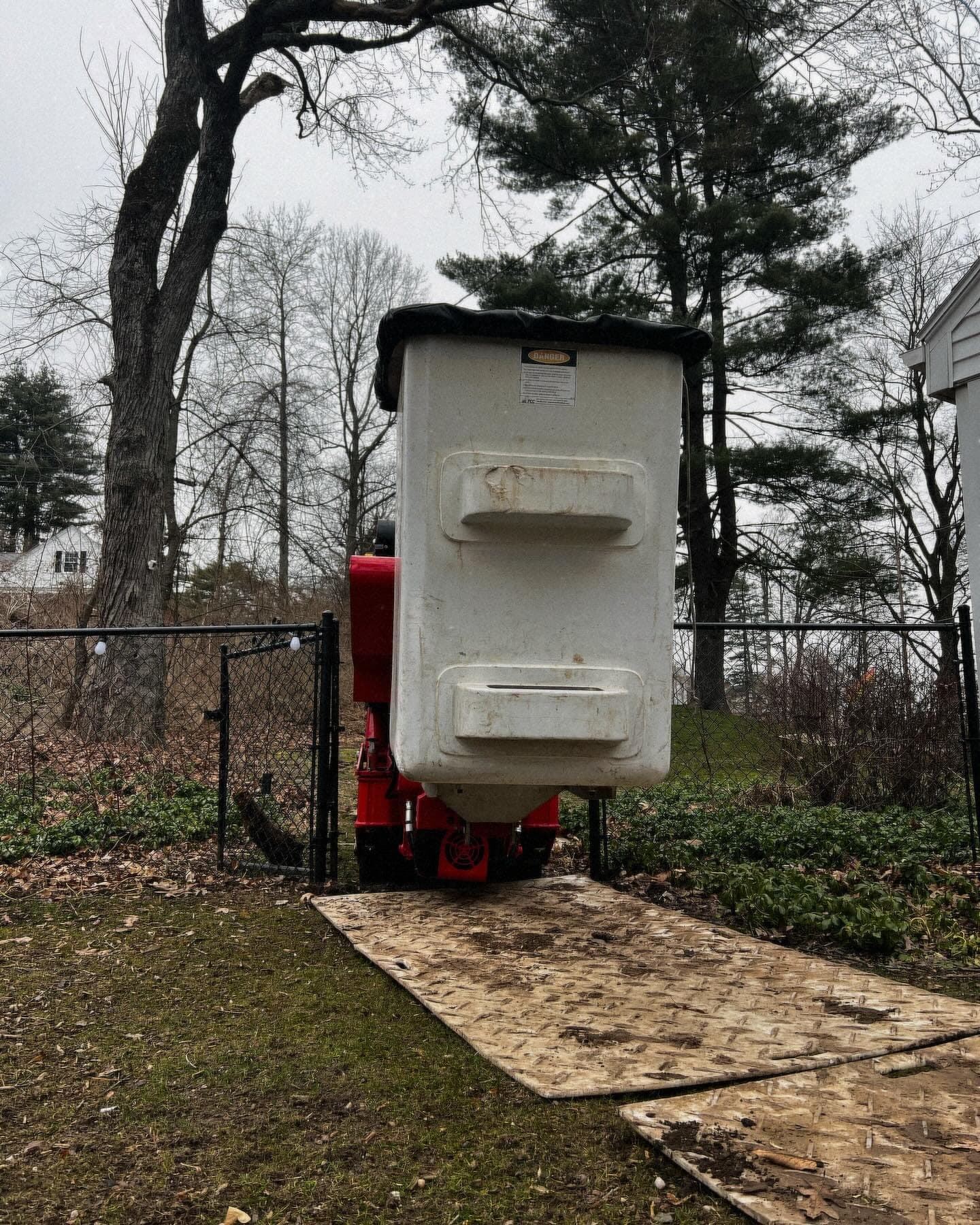 Spider lift bucket raised over a backyard on ground-protection mats