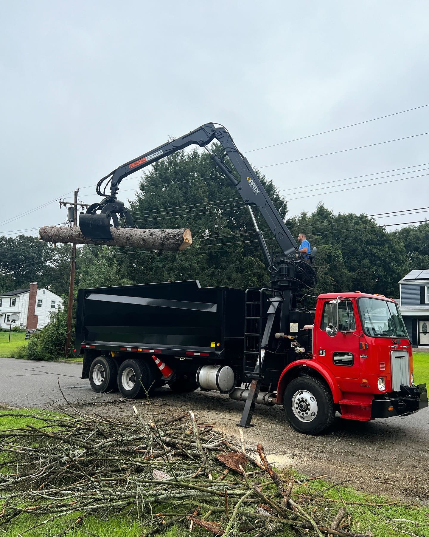 Red grapple truck loading logs from a roadside tree job