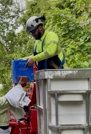 Julian in the spider-lift bucket handing a blue pet carrier down to a helper