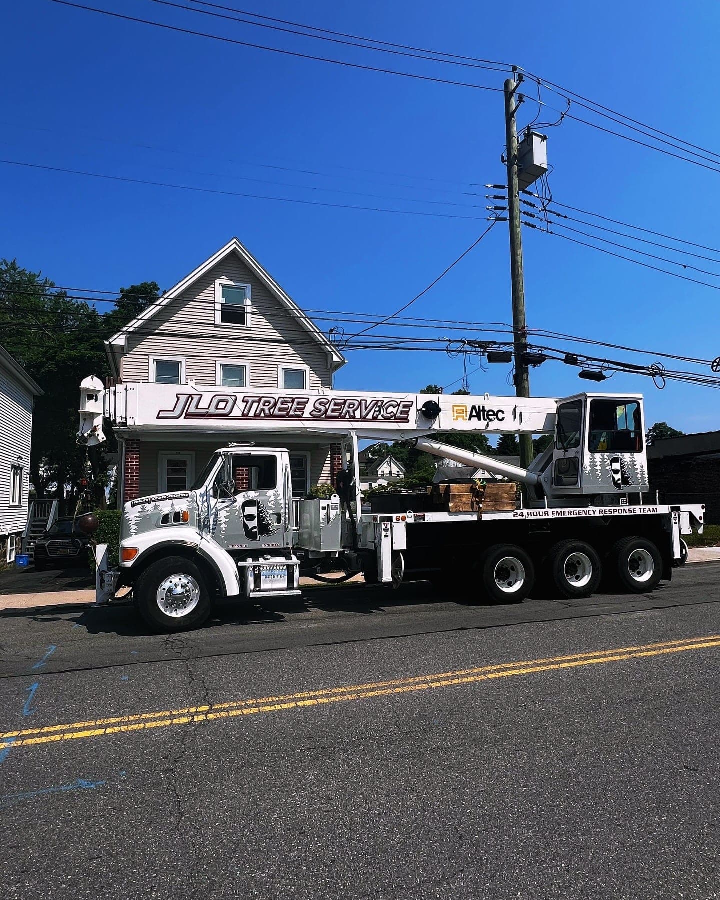 JLO Tree Service crane truck parked on a street beside overhead lines