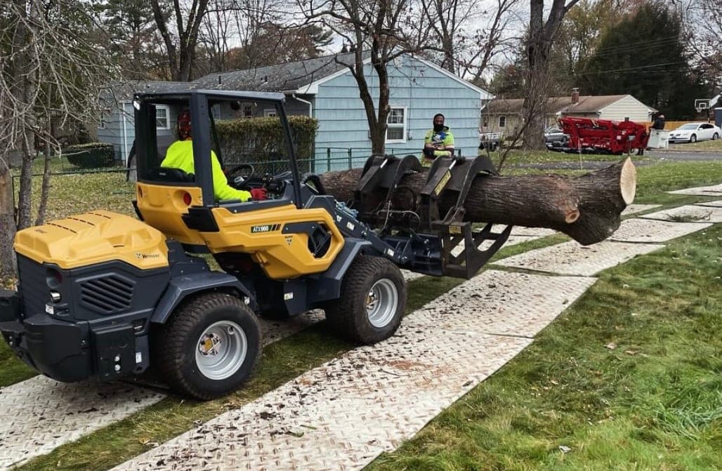 Compact loader carrying a log across a lawn on ground mats