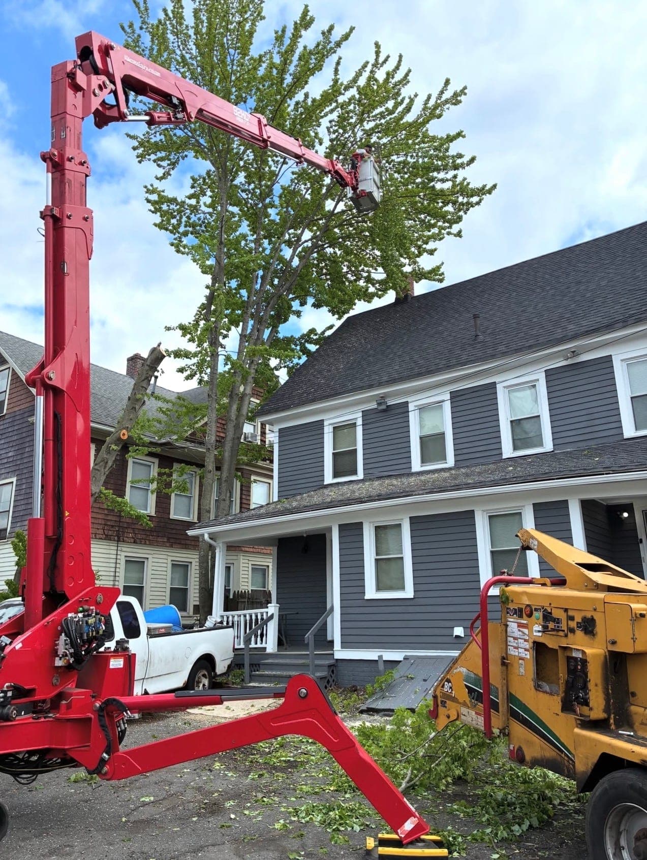Red spider lift reaching over a two-story house, with a chipper in the driveway